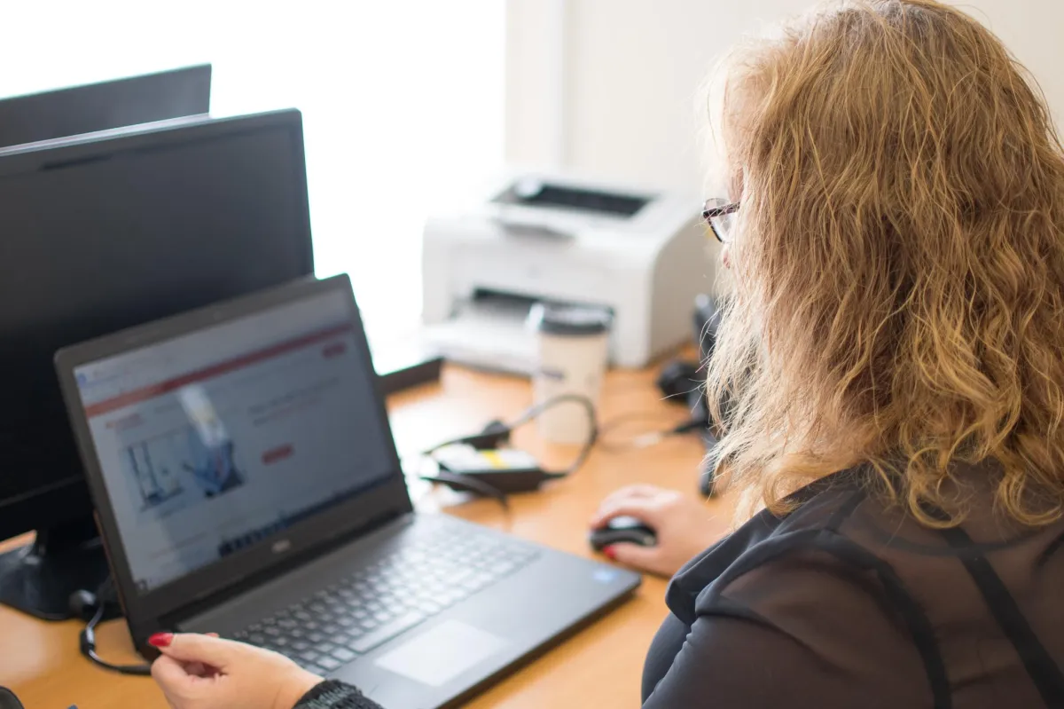 Mortgage advisor with curly blonde hair working on a laptop in a bright office, viewing a mortgage website.
