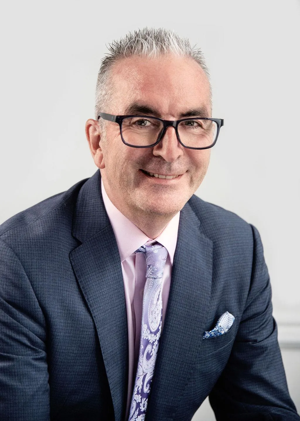 Richard Gill, of Aspect Mortgages in a navy jumper and checked shirt standing against a plain dark background