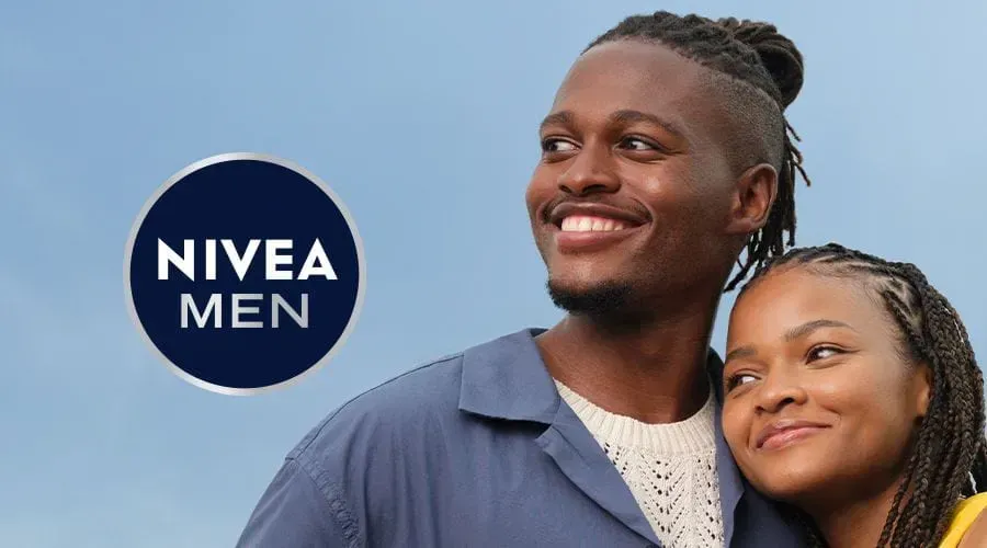 Behind-the-scenes still from a live skincare campaign set featuring Thabang mid-shot with production lights and crew out of focus.