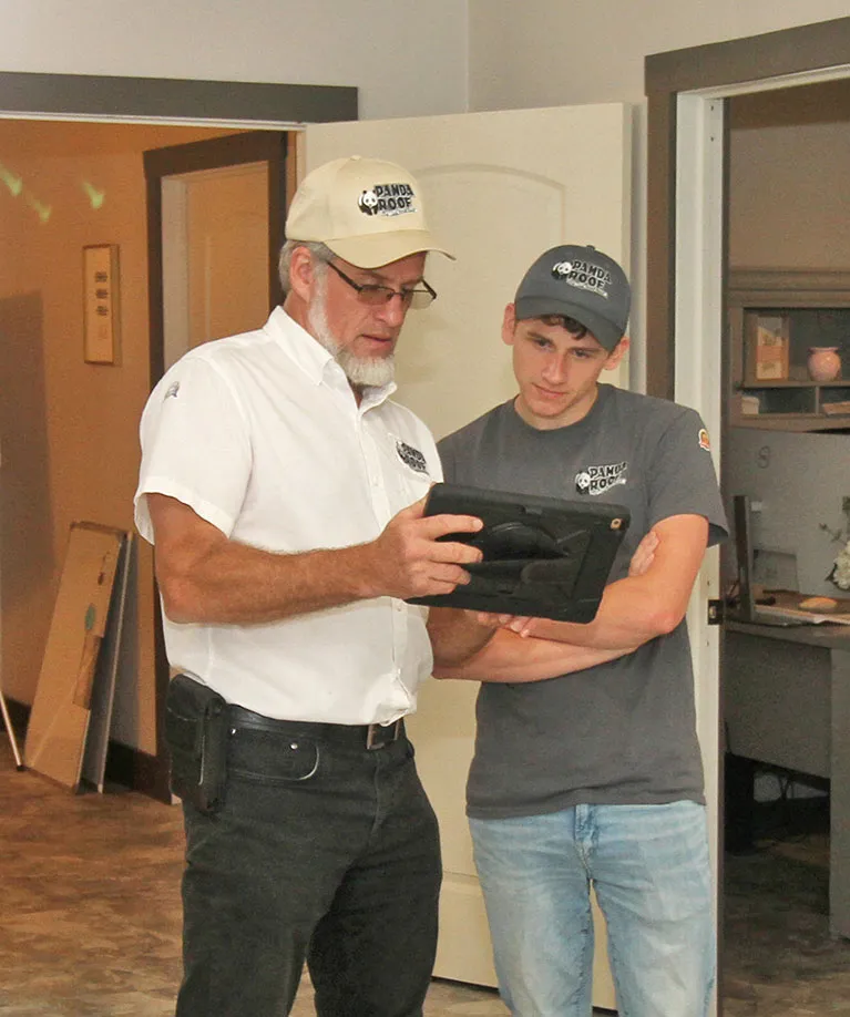 Two male roofing professionals in Panda Roof uniforms reviewing information on a digital tablet