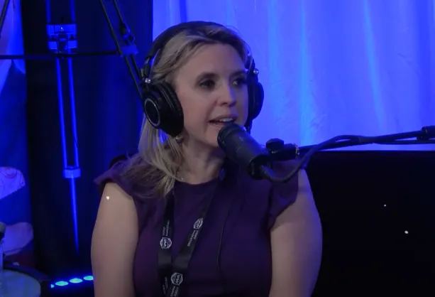 Podcast studio with Jax at a condenser microphone, warm tungsten and teal backlighting, laptop and notes visible.