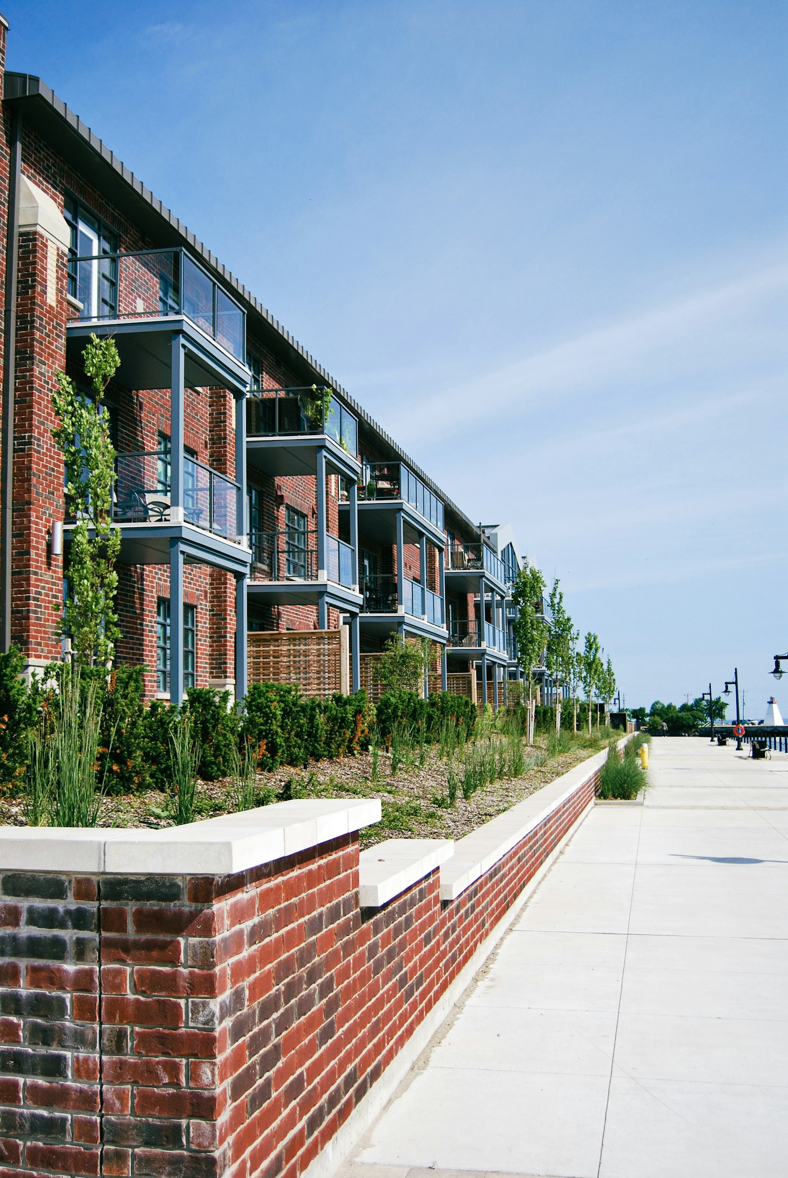 Red brick multifamily apartment building with balconies along a landscaped walkway