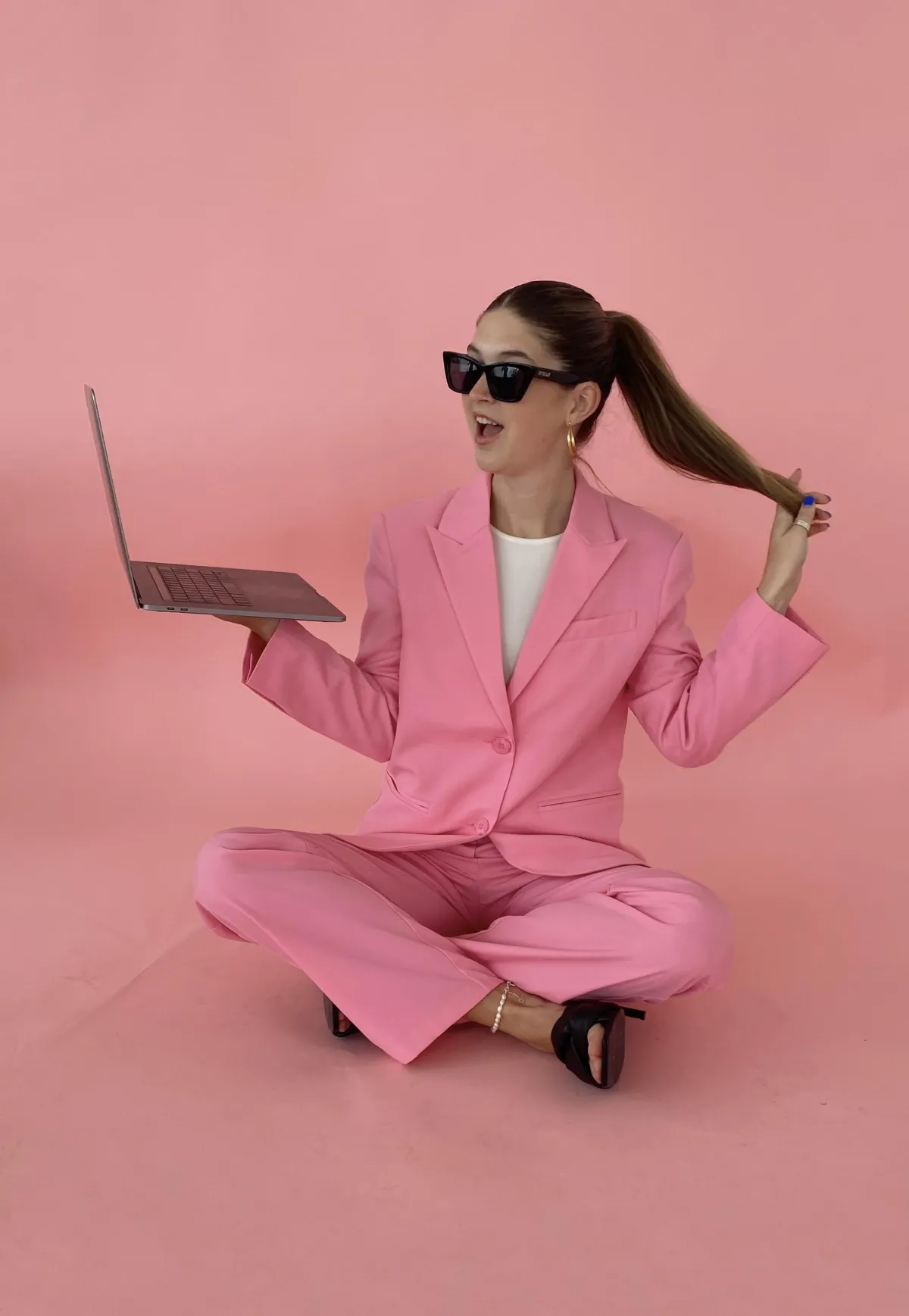 woman holding a laptop in a pink suit with sunglasses on advert for working well club co working sessions
