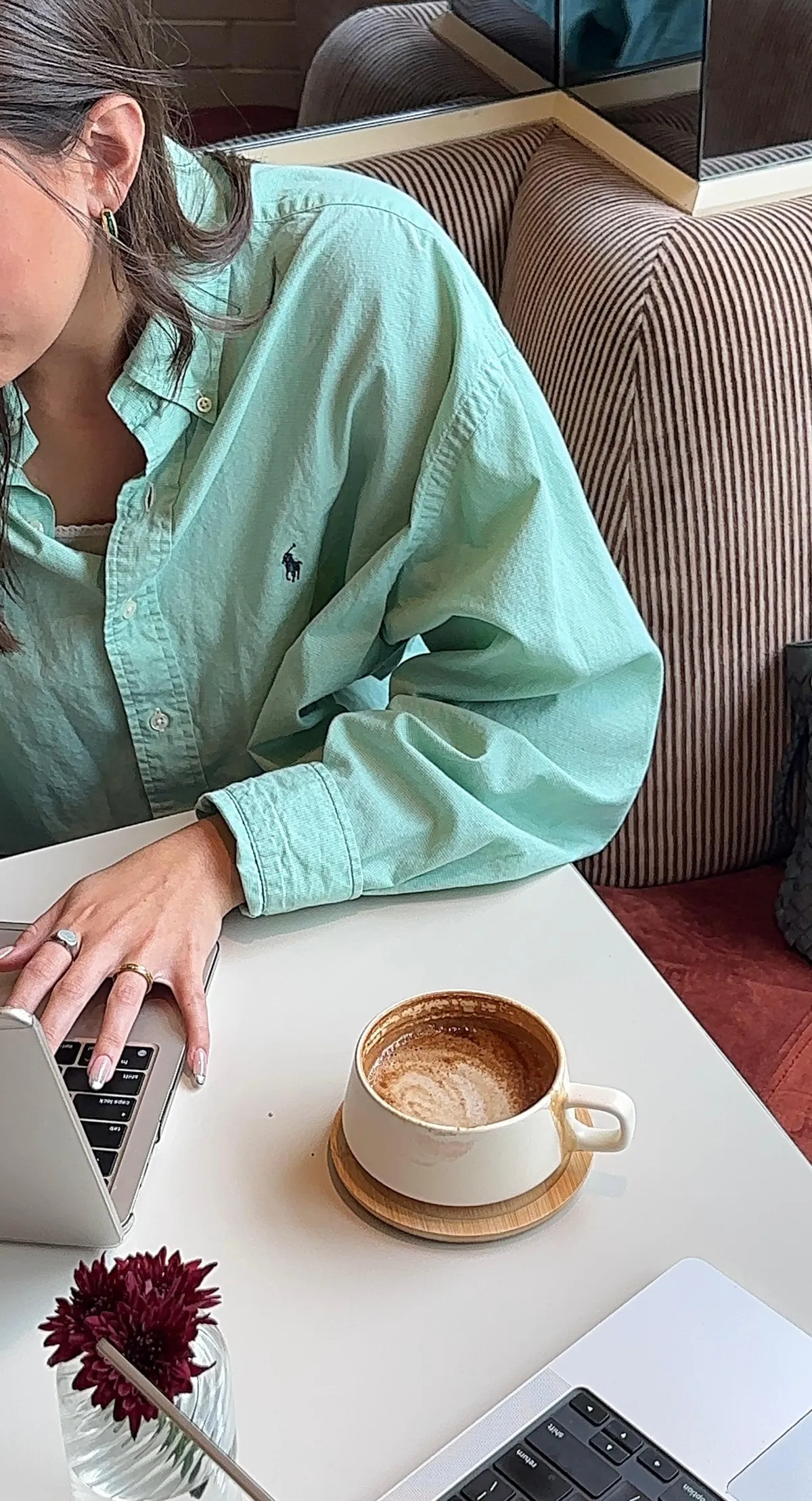 woman in a green shirt working with someone else at a laptop with a coffee
