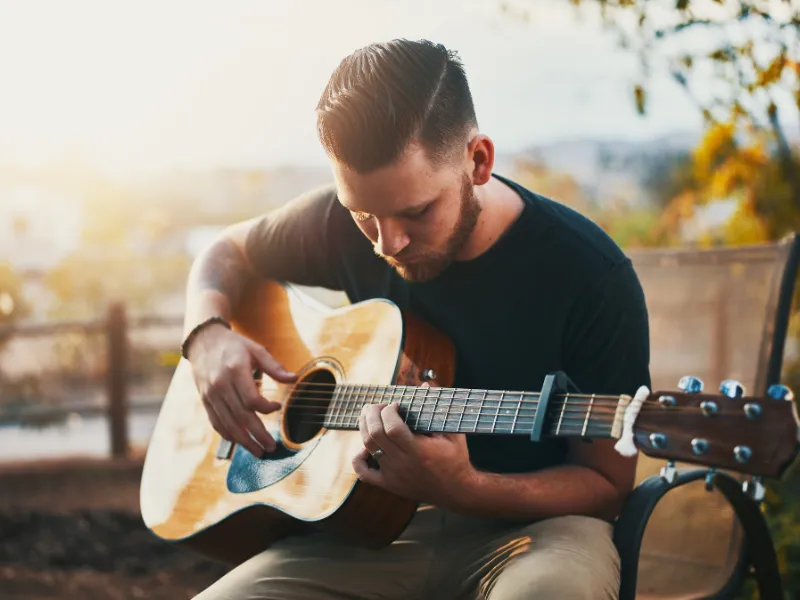 Adult sitting on bench playing guitar