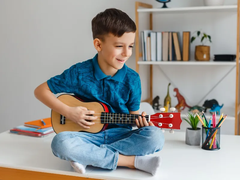 A kid smiling while learning Ukulele at Lochwood Academy. 