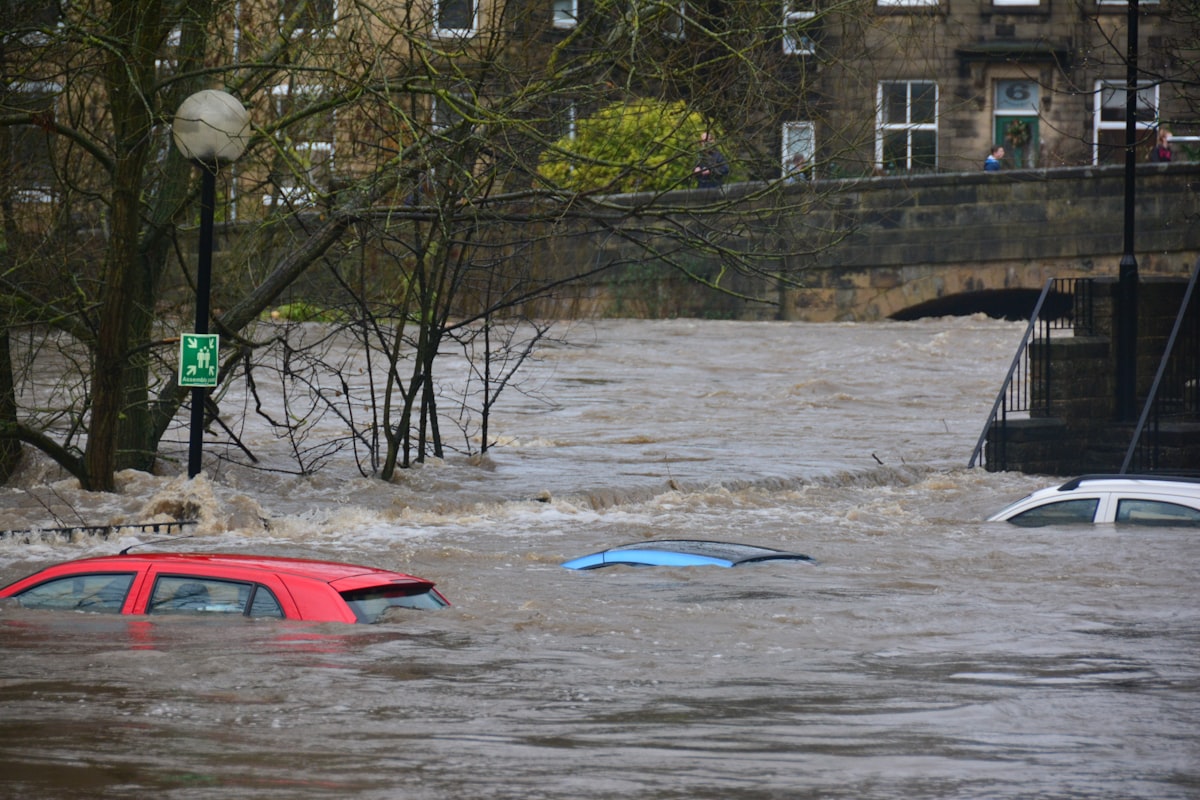 Fast-moving brown floodwater surging through a town street with submerged cars