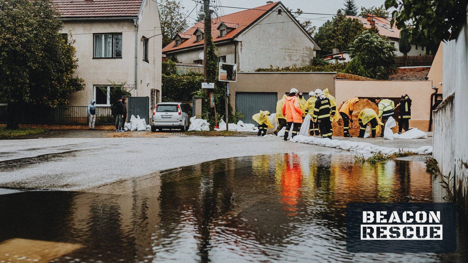 Emergency responders in reflective gear placing sandbags along a flooded residential street