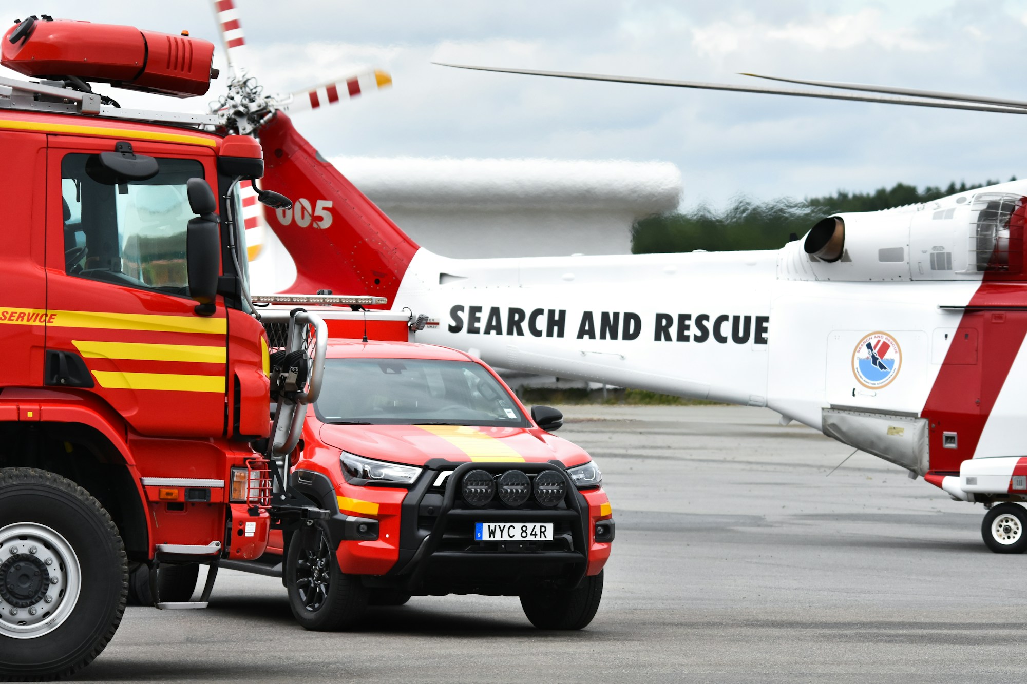 Fire and rescue truck staged beside a search-and-rescue helicopter on an airport tarmac, ground and air assets ready for coordinated deployment