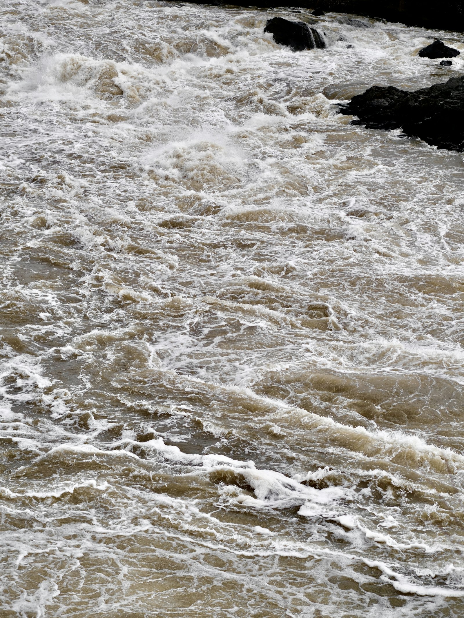 Fast-moving muddy flood water churning over rocks in a swollen river
