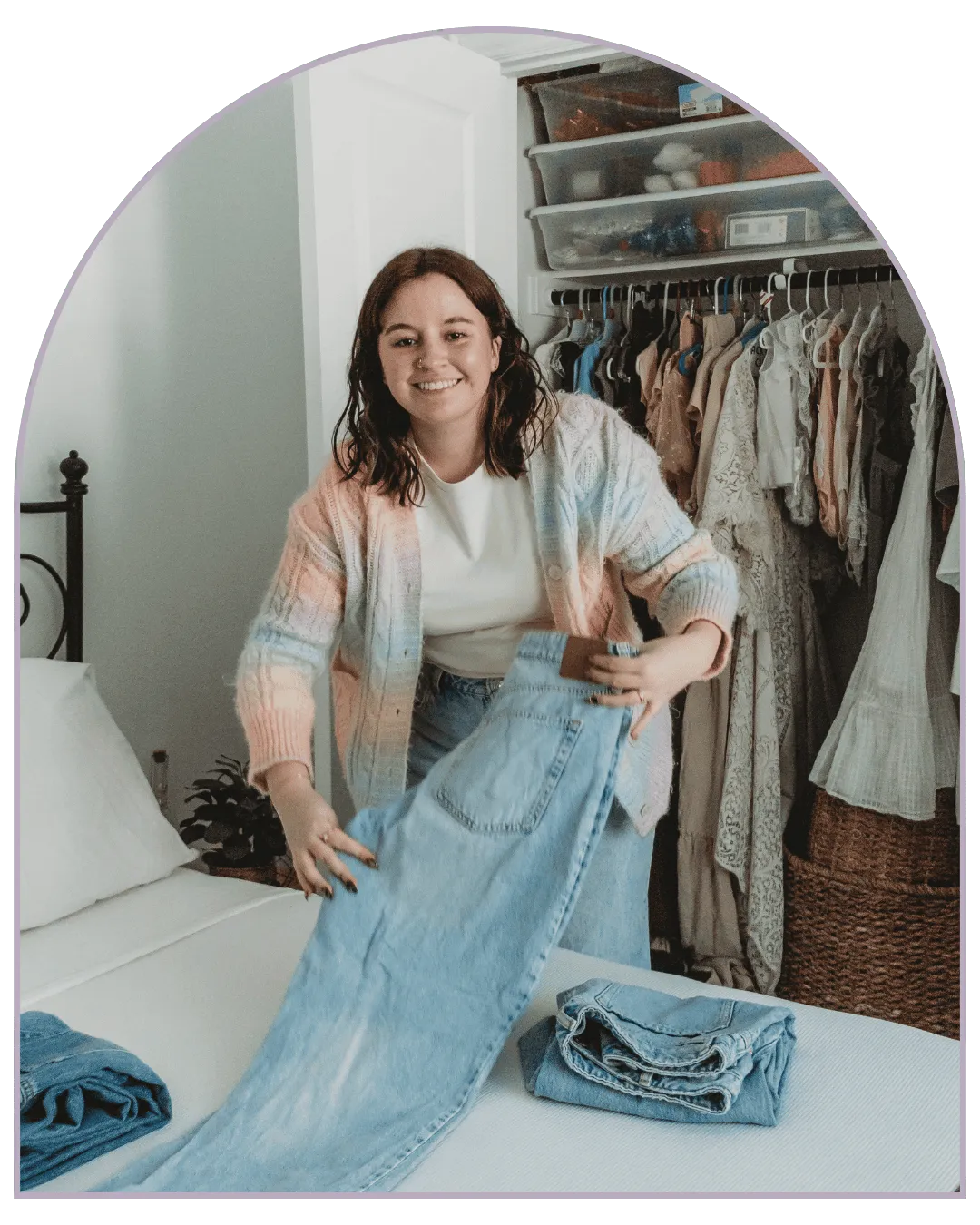 Professional home organizer folding jeans on a bed in front of a neatly organized bedroom closet