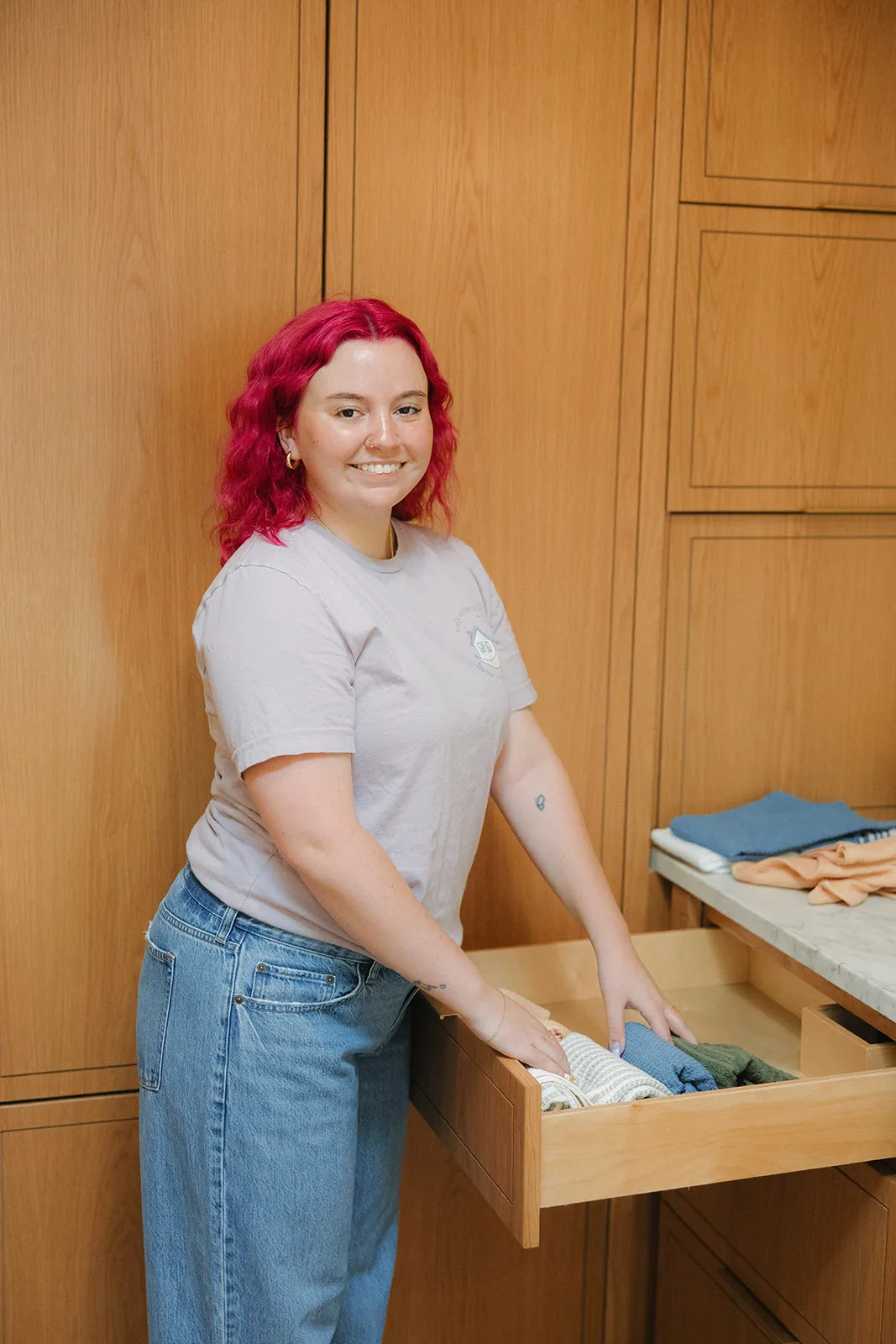 Jamie McPhaul, Austin professional organizer, smiling while organizing folded kitchen towels in a drawer