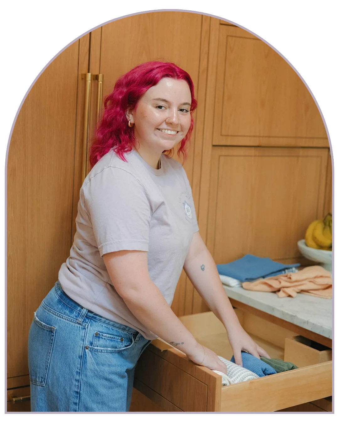 Jamie McPhaul, founder of Tidy Crescent Co., smiling as she tucks folded dish towels into a wood kitchen drawer