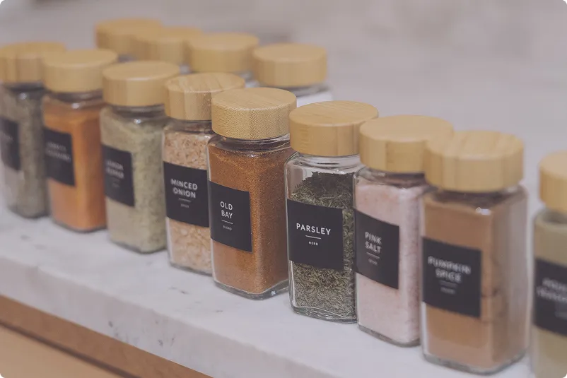 Tidy Crescent Co. spice organization with matching glass jars, bamboo lids, and black labels on a marble counter