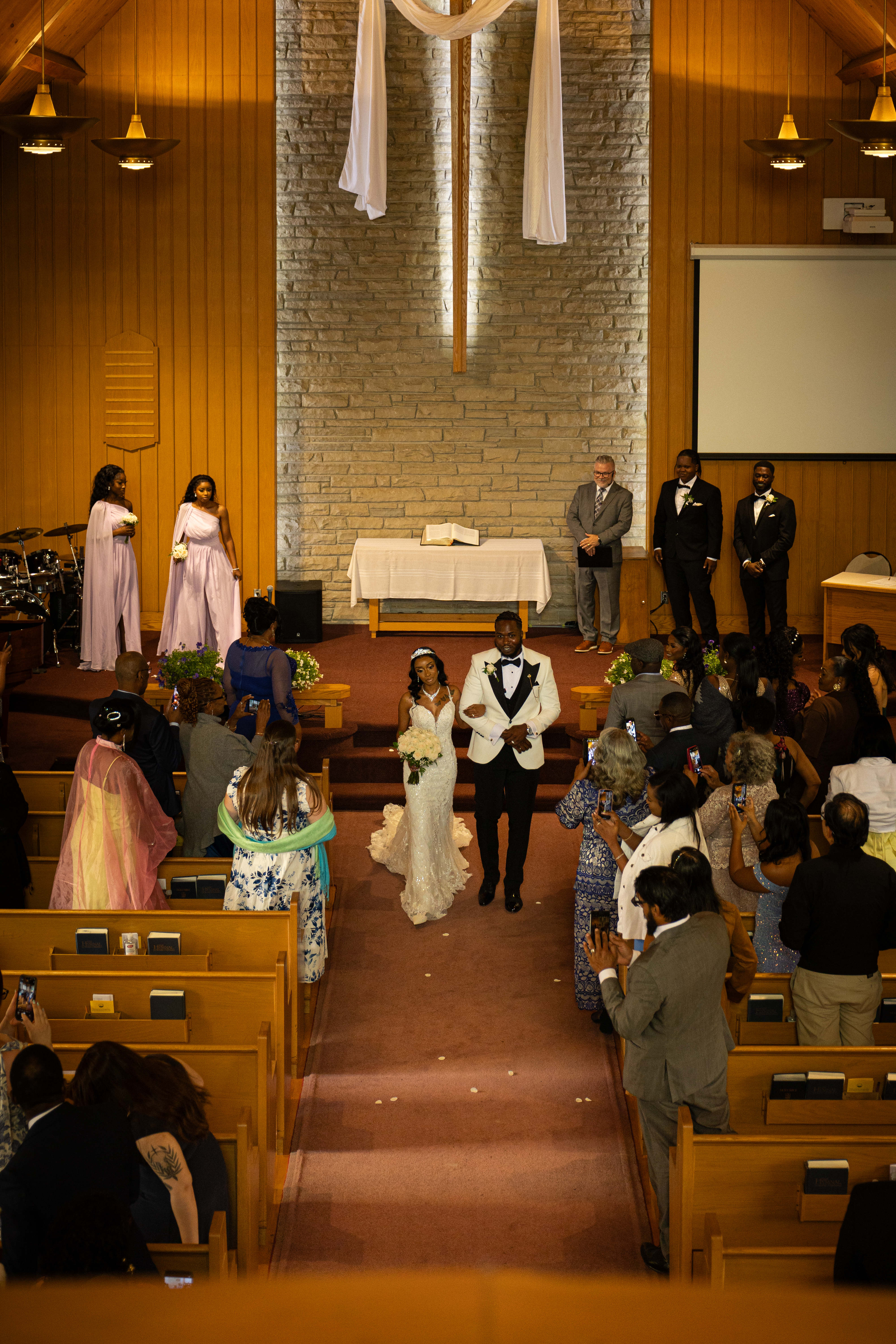 A white flower with green leaves in front of a brick wall