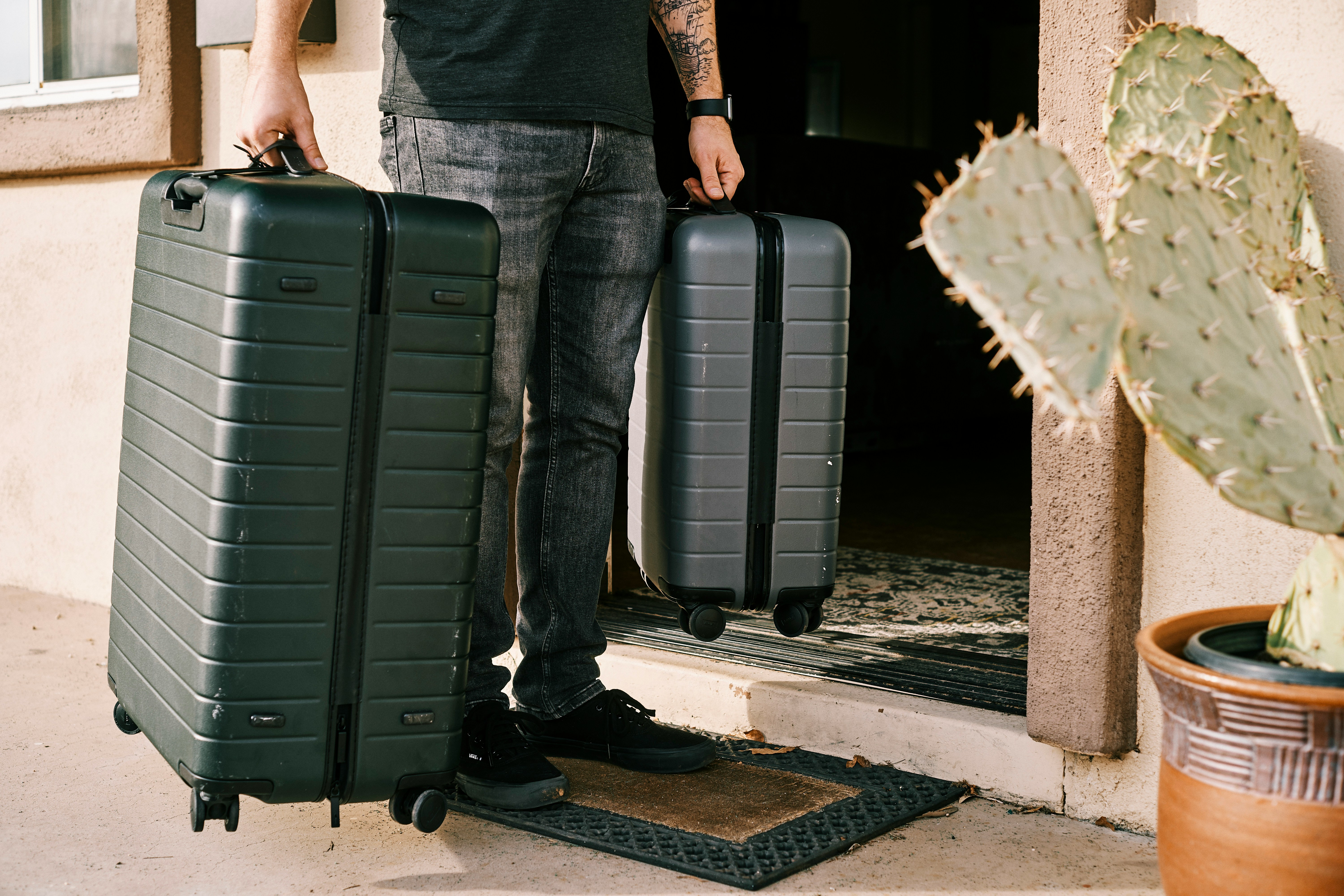 Person holding two hard-shell suitcases outside front door preparing for family vacation