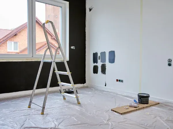 Interior painting in progress with ladder, paint samples, and black wall section
