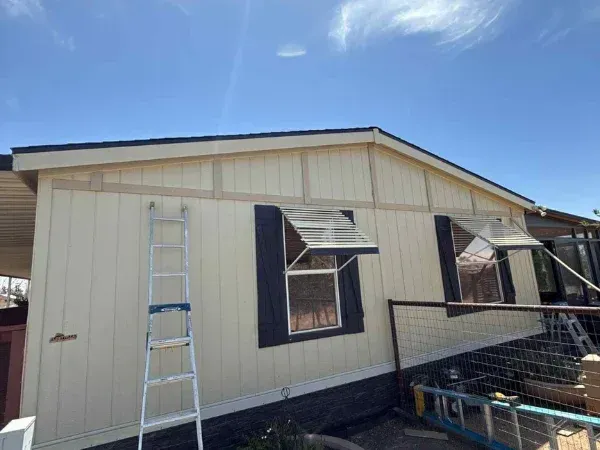 Exterior house painting in progress with ladder against wall and shutters open