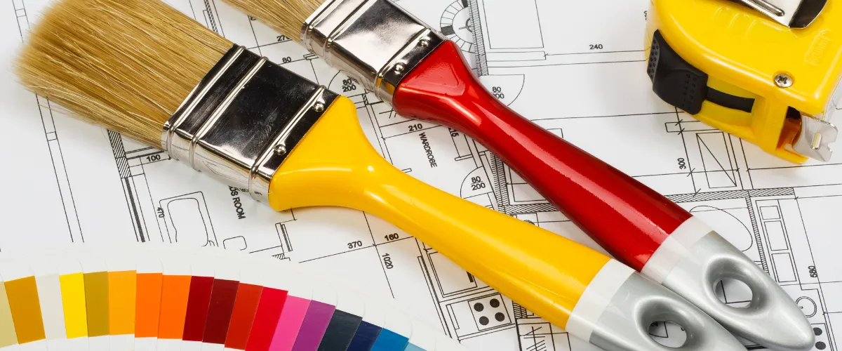 Paintbrushes, color palette, and tape measure on blueprint for home painting project