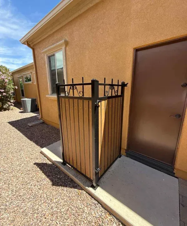 Custom wooden and metal trash bin enclosure installed beside home exterior wall 