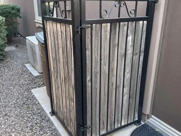 Outdoor wooden and metal gate enclosure beside house with decorative iron frame.