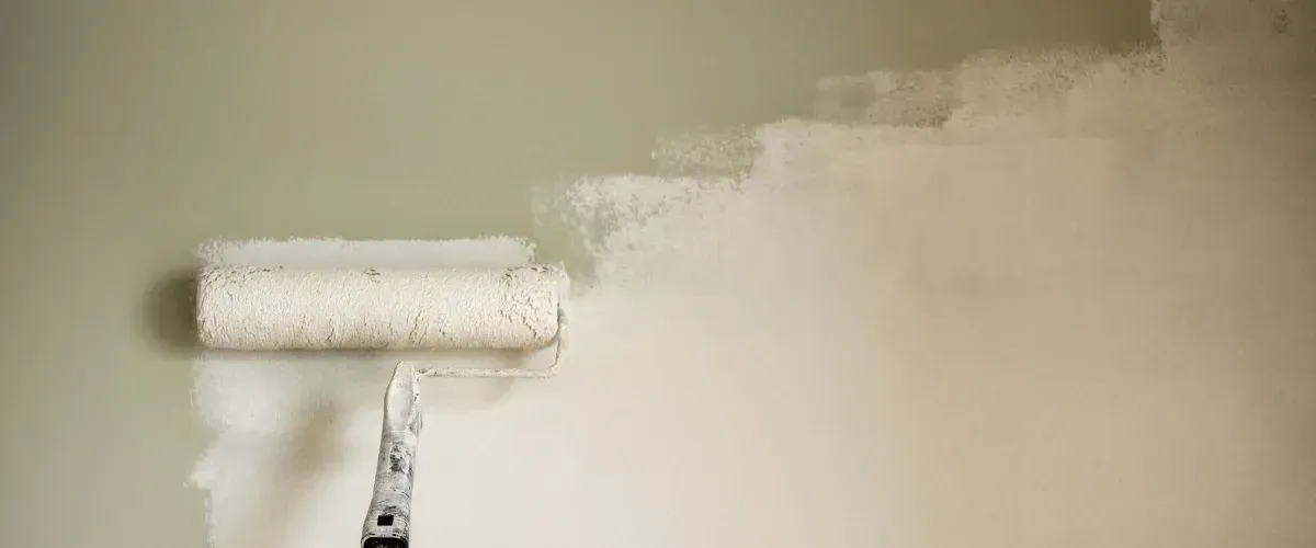 Close-up of paint roller applying fresh coat of light paint on wall.