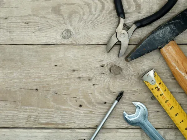 Collection of hand tools including pliers, hammer, screwdriver, wrench, and measuring tape on a wooden surface.
