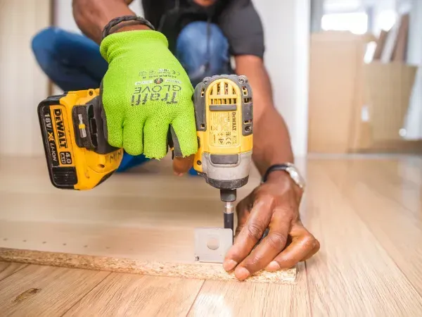 Close-up of a worker using a power drill to secure hardware during furniture assembly.