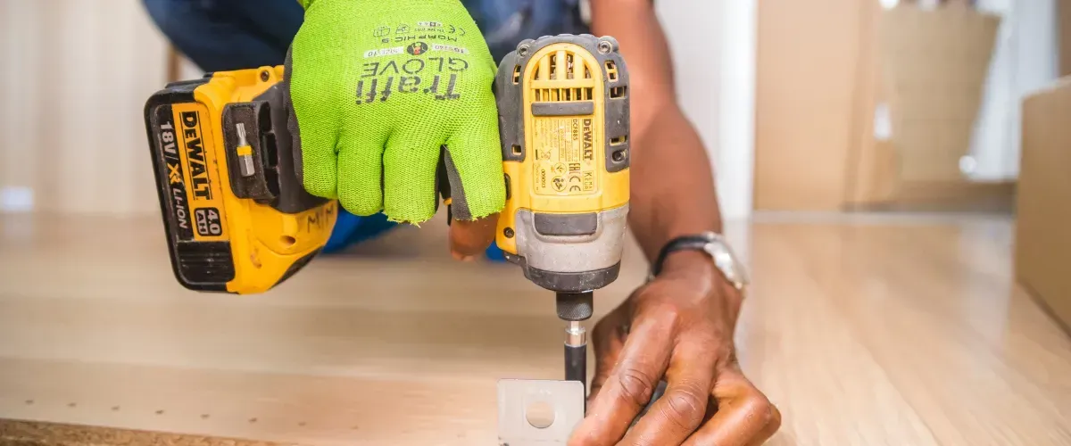 Handyman assembling furniture with a yellow power drill and protective gloves.