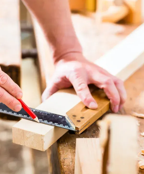 Carpenter measuring and marking wood with square and pencil for precision cut