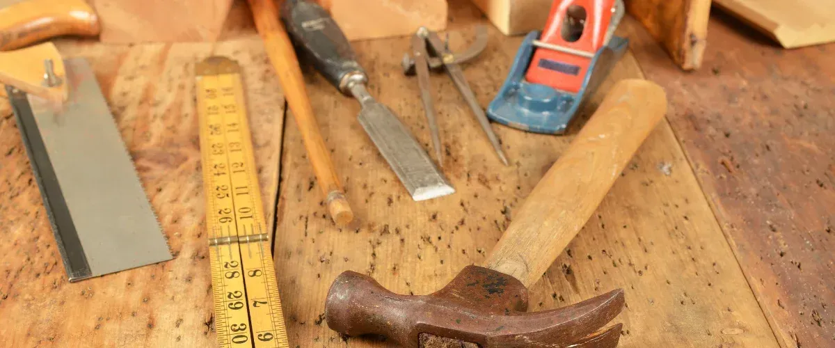 Carpentry tools including hammer, saw, ruler, and chisels on a woodworking bench