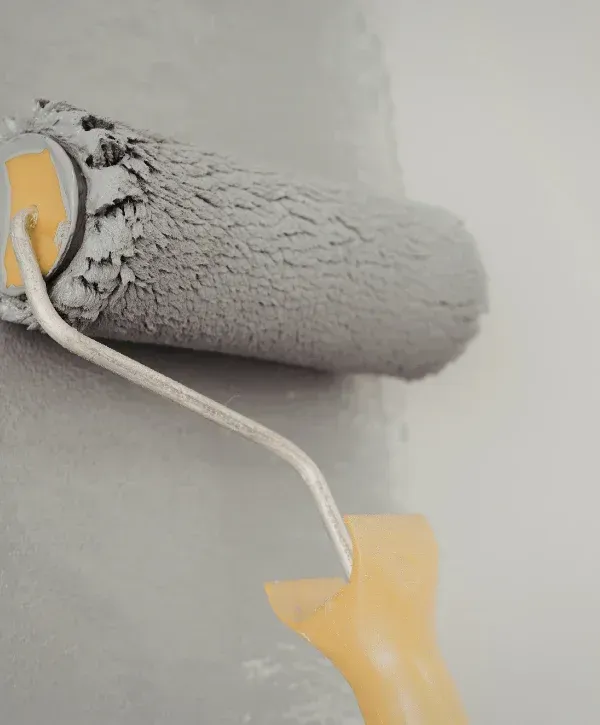Close-up of a paint roller applying gray paint smoothly to a wall surface.