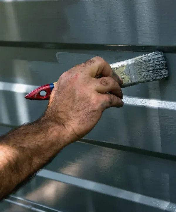 Close-up of hand painting metal siding with brush for home improvement.