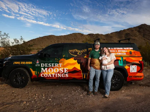 A family of three standing proudly next to their Desert Moose Coatings truck in a desert landscape.