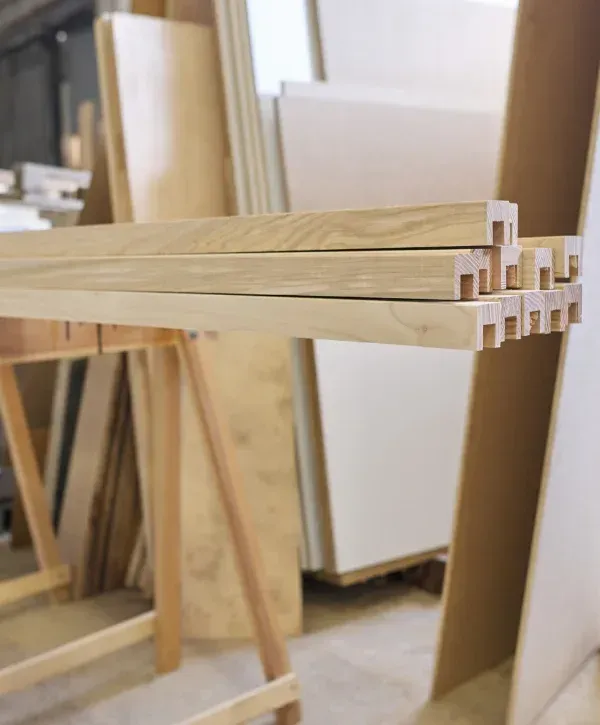 Light wooden slats with precisely cut grooves stacked on a workbench in a bright carpentry workshop.measuring and marking wood with square and pencil for precision cut