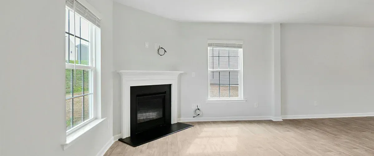 An empty room prepared for renovation with a ladder, paint buckets, and covered furniture near a large window.