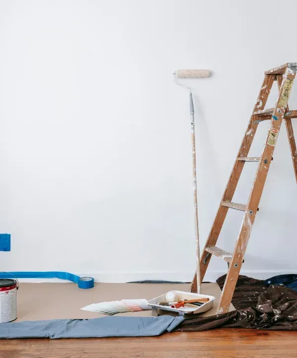 A newly painted white wall, with a ladder, paint roller, color swatches, paint cans, and brushes on the floor.