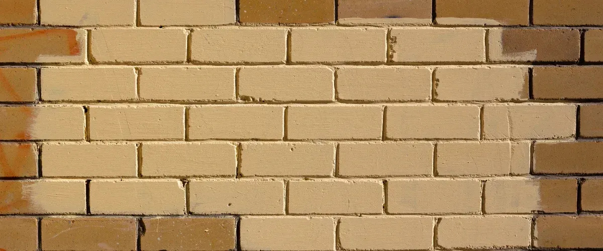 A close-up of a tan brick wall with a few darker brown bricks at the top and bottom edges.
