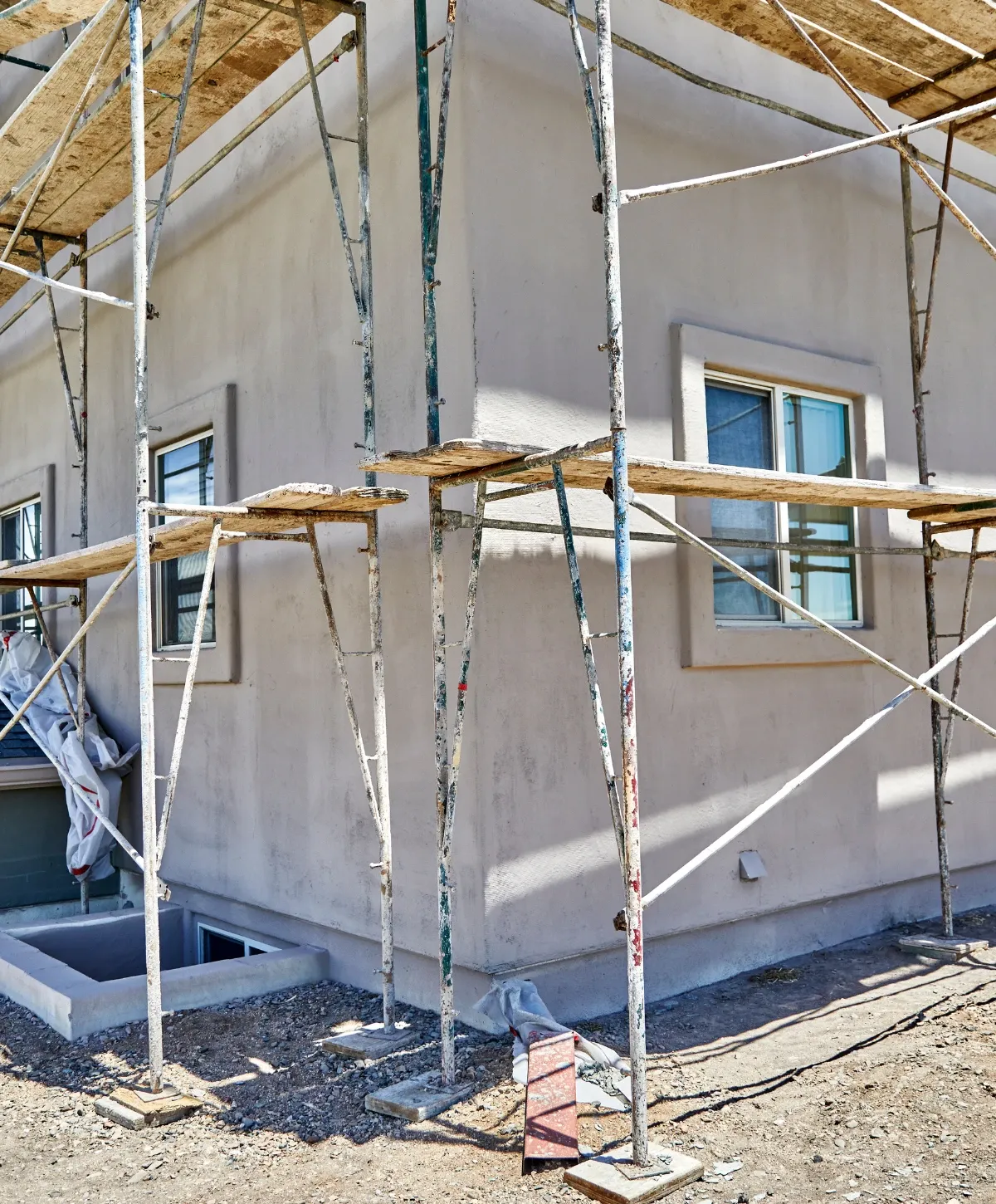 Scaffolding against the light gray wall of a building under construction, showing windows and a foundation opening.
