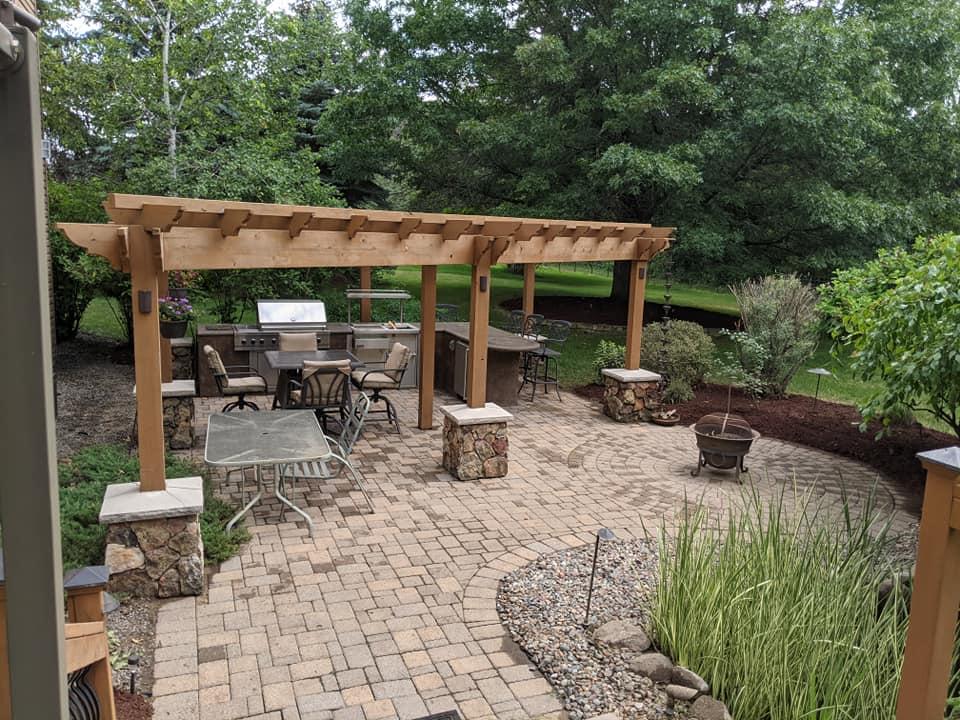 Backyard paver patio with wooden pergola, built-in grill, and fire pit in Minnesota