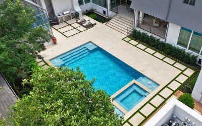 Contemporary backyard pool and spa with light stone decking.