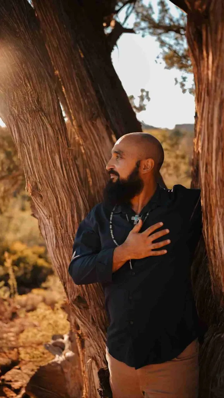Portrait of Michael leaning against a tree at sunset, looking off at the scenery.
