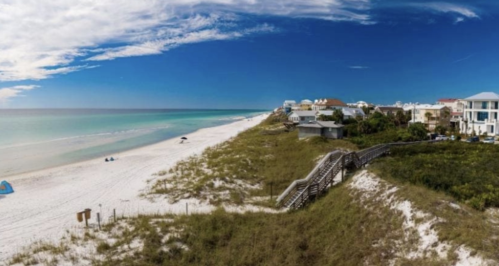 Aerial view of Inlet Beach, Florida showing white sand dunes, turquoise Gulf waters, beachfront homes, and a wooden boardwalk leading to the beach.