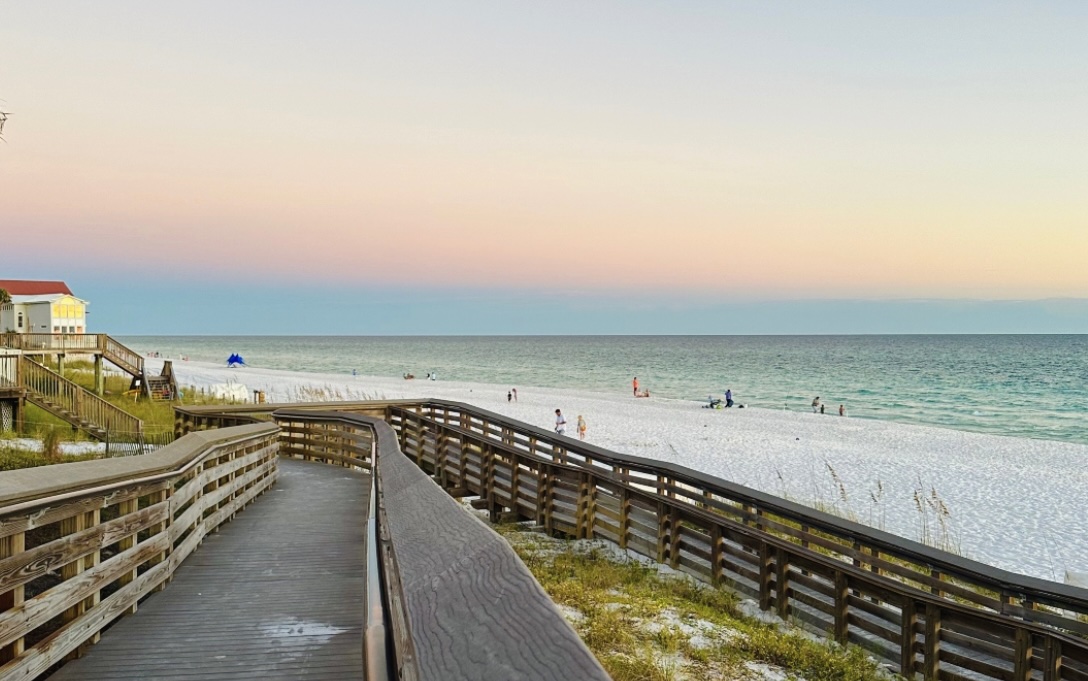 Wooden beach boardwalk leading to the shoreline at Dune Allen Beach, Florida with white sand, Gulf waters, and coastal homes at sunset