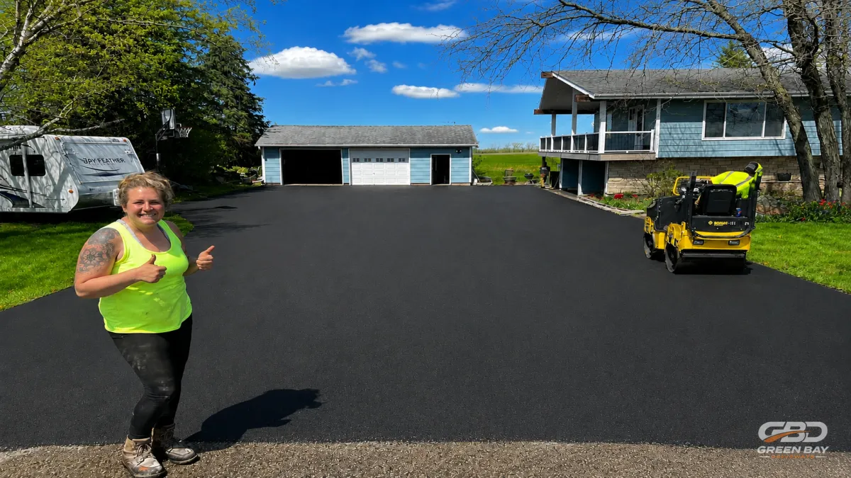 Worker operating roller to complete final finishing passes on asphalt driveway