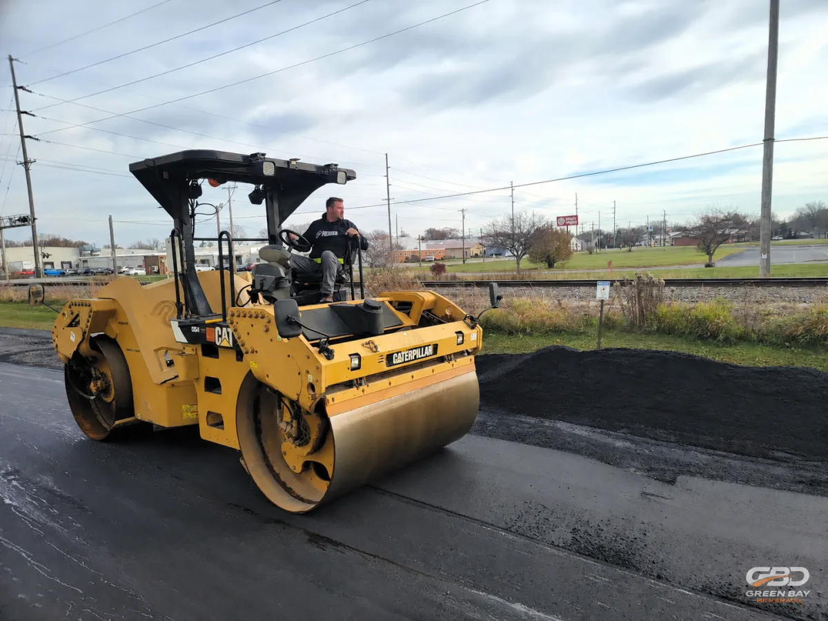 Worker giving thumbs up beside freshly paved asphalt driveway project