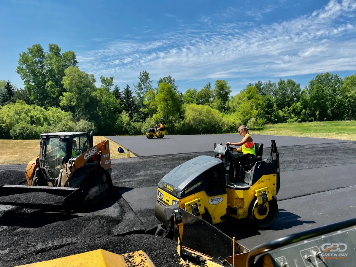 Asphalt paving crew compacting and shaping asphalt with skid steer and rollers