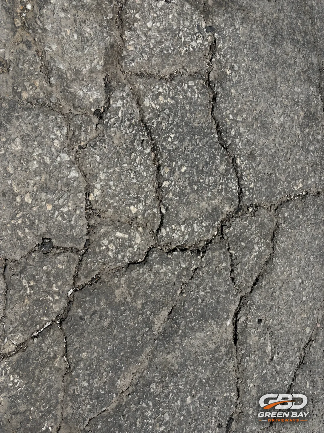 Close-up of cracked asphalt driveway surface showing weathered pavement damage before driveway repair.