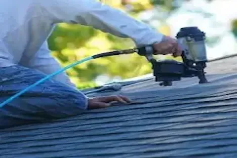 Roofer nailing down shingles with pneumatic nail gun during roof repair service