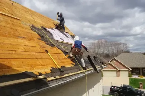 Two-man crew tearing off old shingles during roof replacement in Brooklyn Park by Brooklyn Park Roofing Co